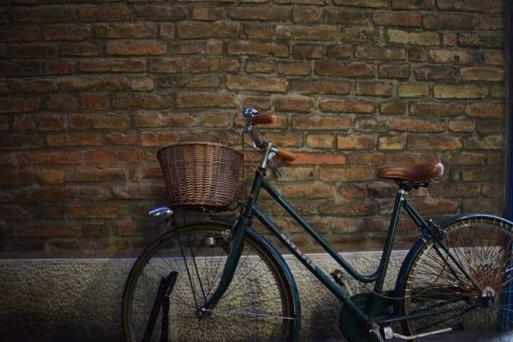 A bike with a basket leaning against an exposed brick wall.