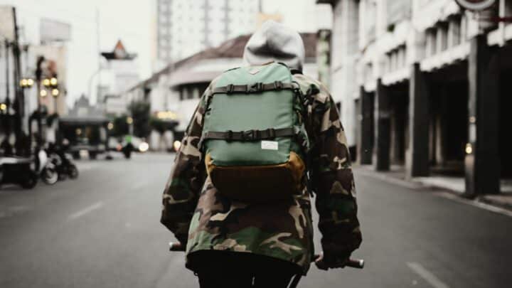 Viewed from behind, a cyclist wearing a green backpack rides through the city.