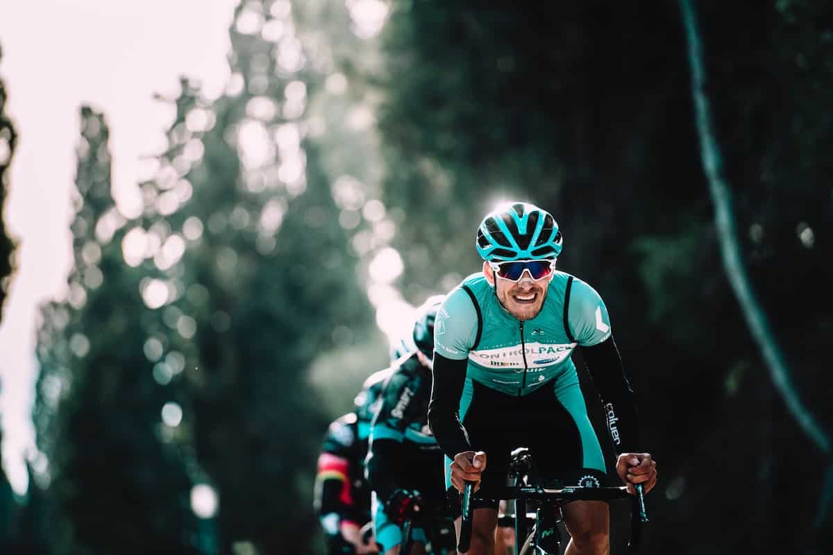 An older cyclist leading a pack in teal jerseys.