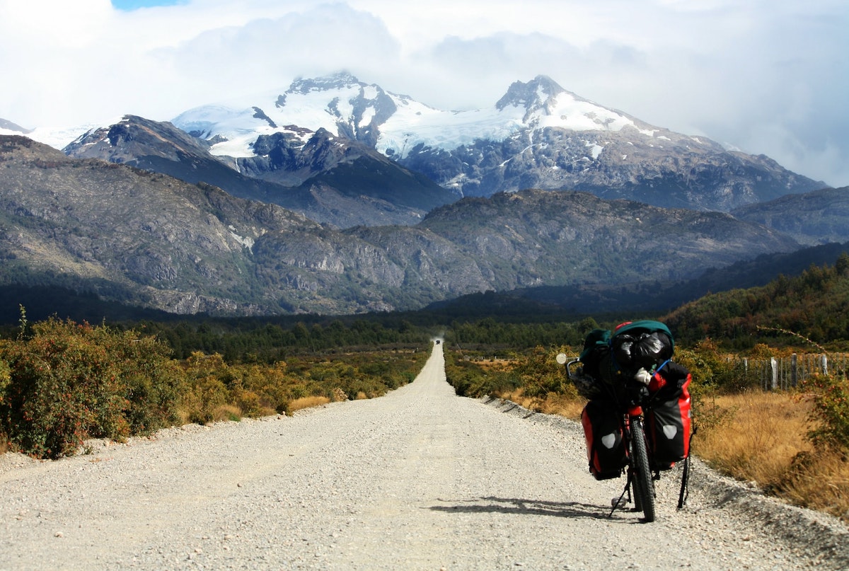 A bike on a dirt road with two packed pannier bags; a picturesque mountain view in the background.