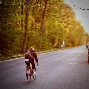 A woman wearing a cycling backpack rides towards the sunrise on a long road.