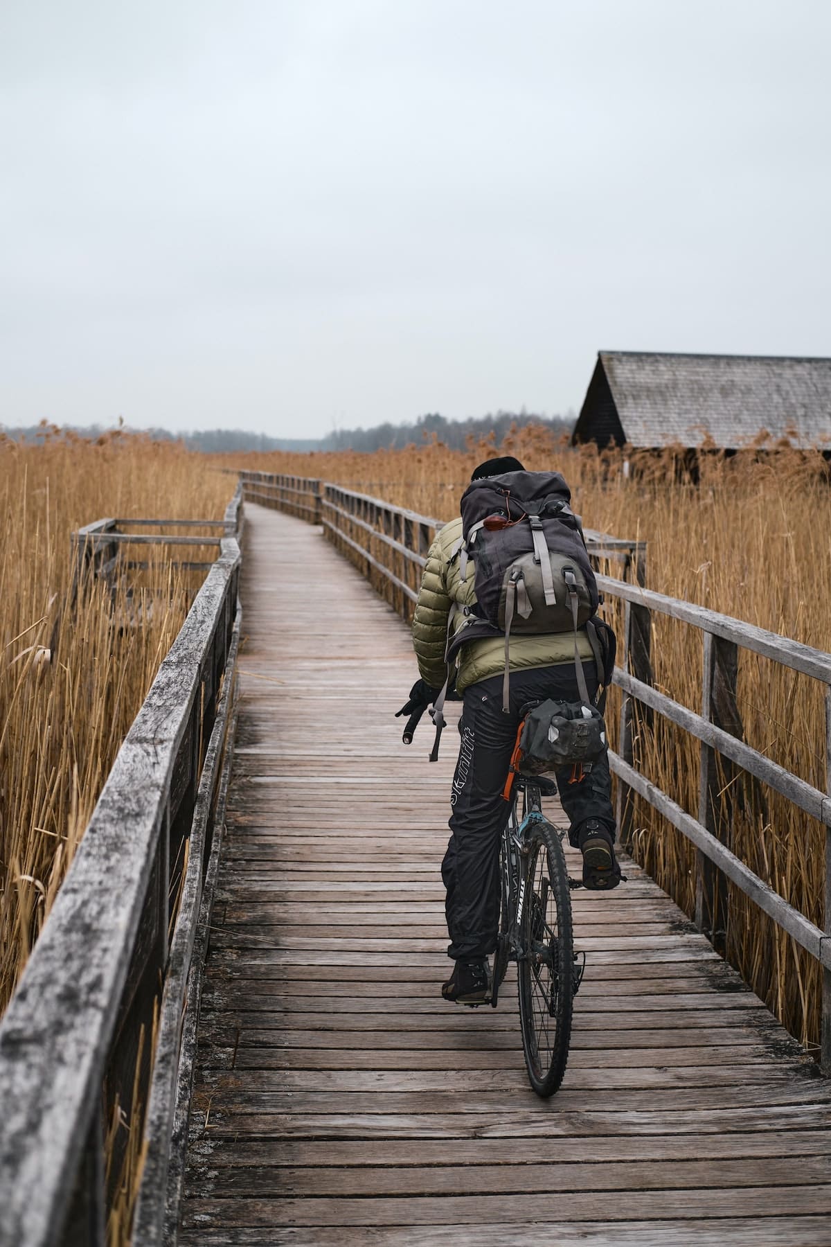 A man wearing a cycling backpack while riding over a wooden bridge in a field.