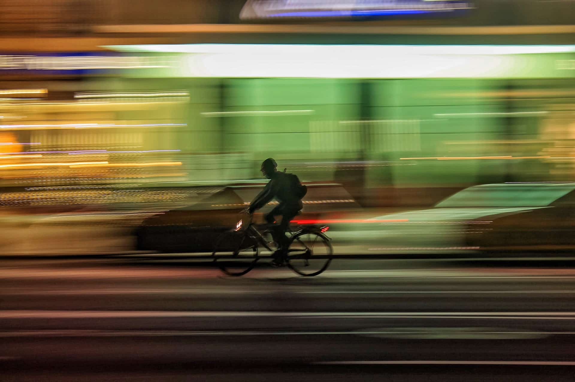 A bicycle riding fast through traffic, it's light streams are visible. 