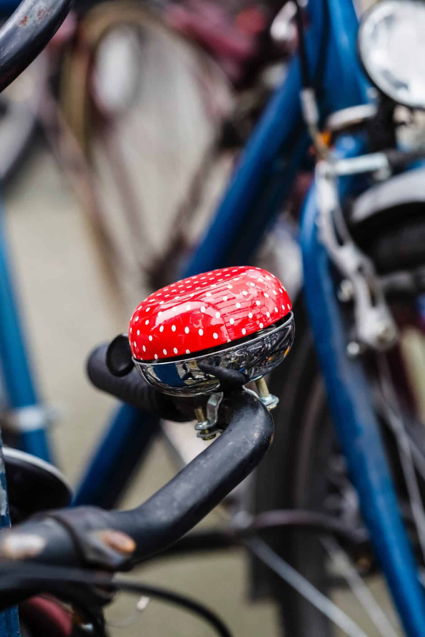 A bright red bell on a black bicycle handlebar.